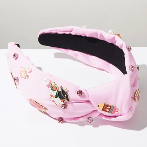 Detail of pink knotted headband with enamel pencil, pearl and graduation charms