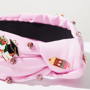 Detail of pink fabric headband with graduation cap, pencil charms, and pink rhinestones