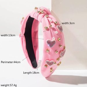 Dettaglio fascia rosa annodata con strass a cuore, perle e borchie dorate