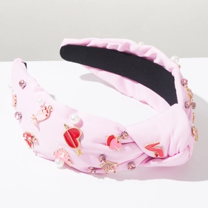 Detalle de diadema rosa con nudo, dijes de corazón, tacones esmaltados y perlas mixtas