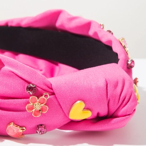 Detalle de diadema rosa con nudo, dijes de corazón esmaltados y brillantes de strass