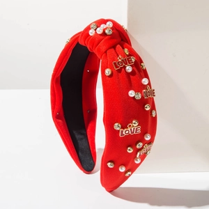 Dettaglio cerchietto rosso annodato con lettere LOVE dorate, perle e strass