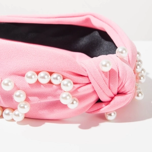 Détail du serre-tête en tricot rose orné de perles élégantes et d'un nœud supérieur