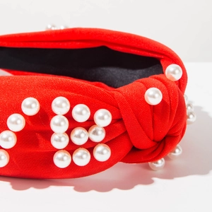 Détail macro du serre-tête noué rouge avec perles blanches formant le mot LOVE