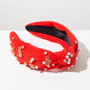 Dettaglio fascia rossa annodata con perle, strass e ciondoli dorati LOVE in rilievo