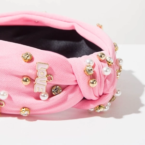 Dettaglio cerchietto rosa con strass, perle e ciondolo LOVE dorato di qualità