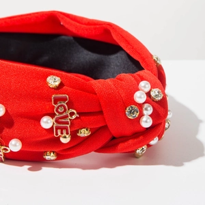 Dettaglio ravvicinato del cerchietto rosso a nodo con perle e ciondolo LOVE dorato
