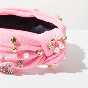 Dettaglio fascia rosa in maglia con strass, perle e un cuore di cristallo