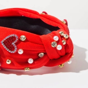 Dettaglio del cerchietto in tessuto rosso annodato con perle, strass e toppa a cuore