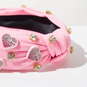 Dettaglio fascia in maglia rosa con cuore di strass e ciondolo con lettera 'LOVE'
