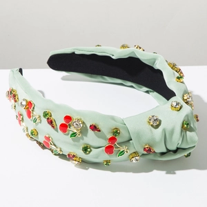 Close-up of a mint green knotted headband featuring red cherry charms and green crystals