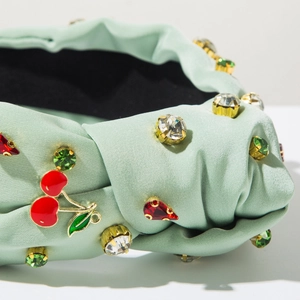 Detail of mint green knotted headband featuring crystal accents and cherry metal charms