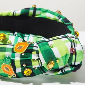 Close-up of green checkered headband with colorful gemstones and orange papaya pendants