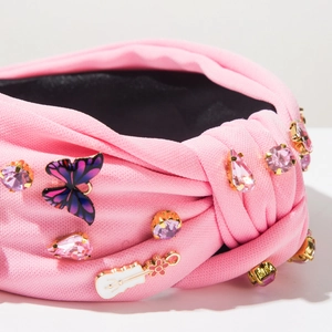 Détail de bandeau rose torsadé avec strass, papillon dégradé et breloques de guitare festive