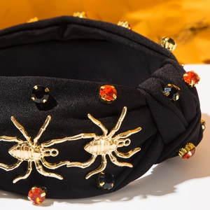 Détail d'un serre-tête noir avec araignée dorée et strass oranges pour Halloween