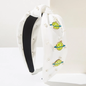 Close-up of white knotted headband with imitation pearls and green Saturn charms