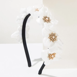Detailed close-up of white floral headband with pearls and rhinestones on black band