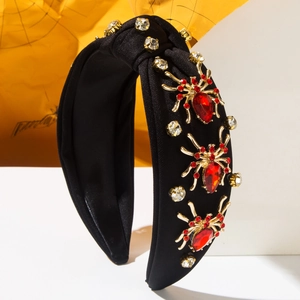 Close-up of gold spider charms with red rhinestones on a black knotted headband