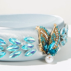 Detail of light blue satin headband with rhinestones and a gold butterfly pearl charm