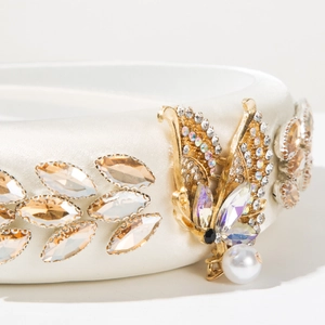 Close-up of white satin headband with gold butterfly, sparkling crystals, and pearl drop