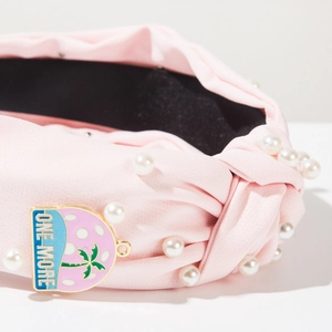 Close-up of pink knotted wide headband with white pearls and ONE-MORE enamel charm detail