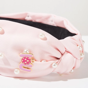 Macro shot of pink fabric headband with faux pearls and enamel metal emblem detail