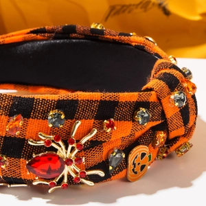 Close-up of Halloween wide headband with spider and pumpkin rhinestones on plaid fabric