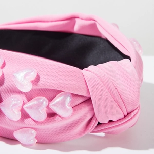 Detailed close-up of a pink knotted headband with sparkling glitter heart accents