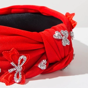 Detailed close-up of red knotted headband with sparkling rhinestones and bow accents