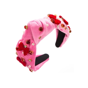 Détail d'un serre-tête en velours rose avec nœuds rouges, strass et perles blanches