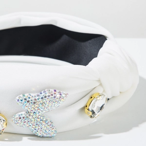 Detail of white fabric headband featuring iridescent rhinestone butterfly and clear gem
