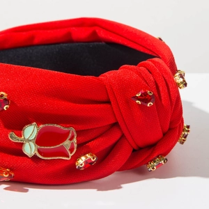 Detailed close-up of red twisted headband with teardrop rhinestones and rose enamel charm