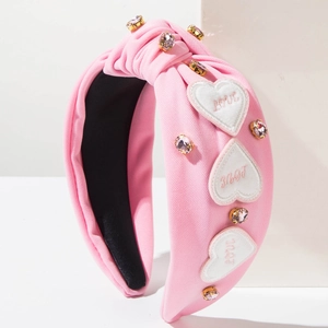 Détail d'un serre-tête rose en tissu avec écussons cœurs brodés et strass scintillants