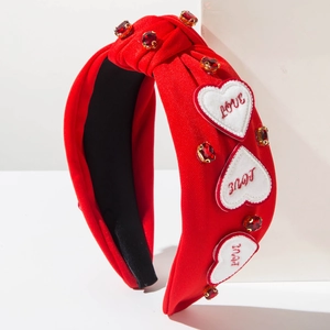 Détail d'un serre-tête en tissu rouge avec broderie Love et pierres précieuses rouges
