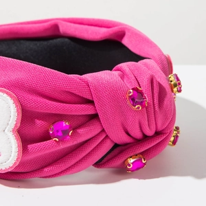 Détail macro du serre-tête rose noué avec strass brillants et patch coeur brodé