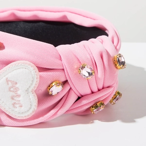 Gros plan sur serre-tête rose en tissu avec broderie Love et détails en strass