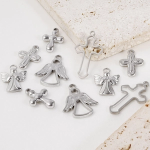 Detailed close-up of 304 stainless steel cross and angel pendants on beige stone surface