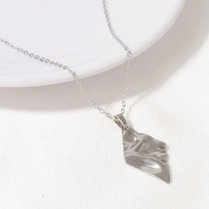 Detailed view of silver diamond-shaped pendant necklace with wrinkled texture on white tray