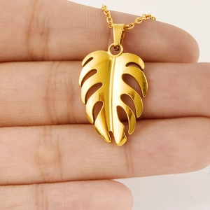 Collier avec pendentif feuille de monstera dorée en acier inoxydable tenu en main