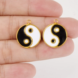 Handheld shot of 304 stainless steel Tai Chi Yin Yang pendants with gold trim and enamel