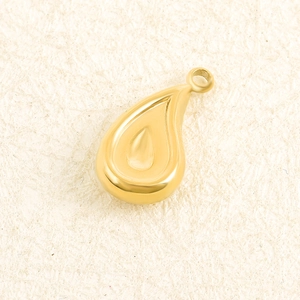 Detailed view of a gold hollow teardrop pendant on a beige textured background