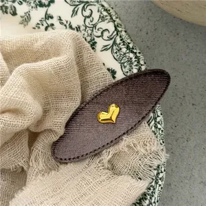 Detailed close-up of brown velvet oval hair clip with gold heart metal accent