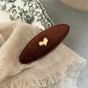 Detailed view of the dark brown fabric hair clip with a gold heart and sewing craftsmanship