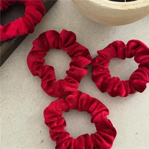 Set of four red velvet scrunchies with pleated texture on marble surface display