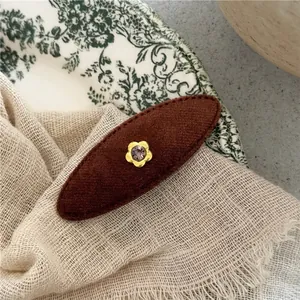 Macro view of brown fabric oval hair clip with gold flower and purple gemstone detail