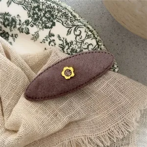 Macro detail of brown oval velvet hair clip with golden flower and purple gemstone inlay