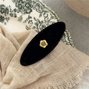 Macro shot of black velvet oval hair clip with gold flower and rhinestone detail