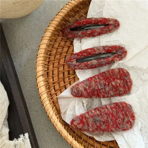 Detail of red and grey knitted hair clips in oval and teardrop shapes on textured paper