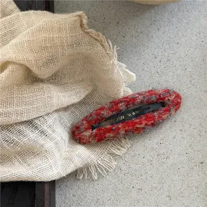 Detailed close-up of a red and gray wool tweed oval BB hair clip on a textured fabric
