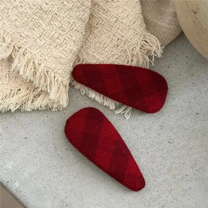 Close-up of red plaid fabric BB hair clips on a soft beige knit blanket surface